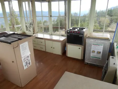 The interior of a fire lookout tower with windows looking out at a forested mountain view.