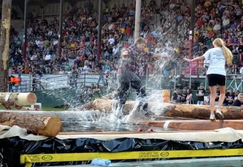 A man and woman log rolling in a pool of water before a crowd.