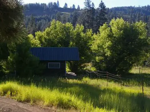 A small cabin nestled in a grassy clearing surrounded by trees and a forest.