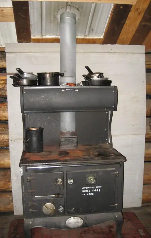 A black wood-burning stove sits inside a cabin with pots on top.