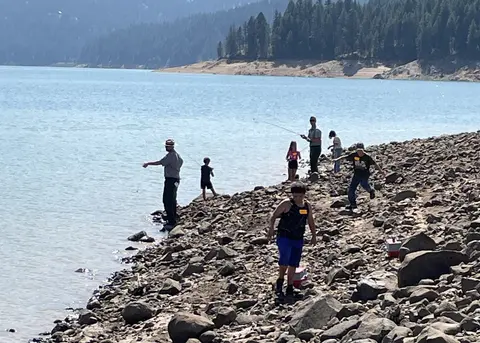 People fishing on a rocky shore by a lake.