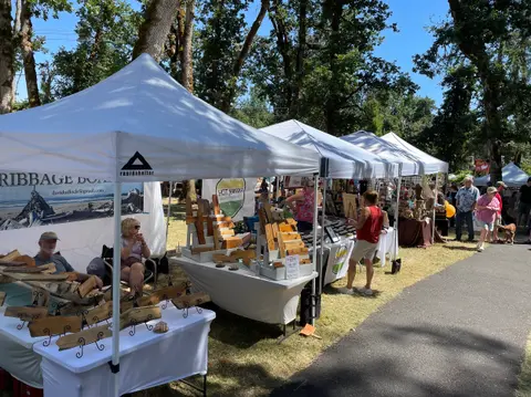 An outdoor market features rows of white tents with vendors selling crafts and goods.