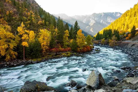 A scenic river flowing through a forested mountain valley with autumn foliage.