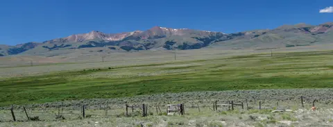 A landscape view showing grassy plains and mountains under a blue sky.