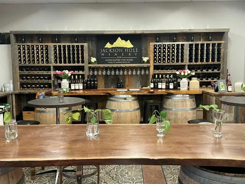 An interior view of a winery tasting room featuring wooden wine racks, barrels, and tables.