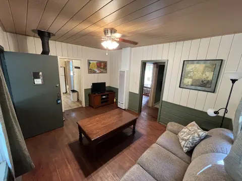 A living room interior with wood flooring, a sofa, coffee table, and doorways leading to other rooms.