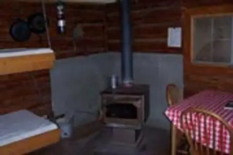 The interior of a rustic cabin featuring a wood stove, bunk beds, and a table.