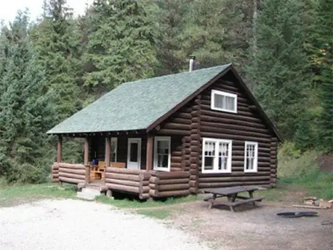 A log cabin surrounded by trees with a picnic table outside.