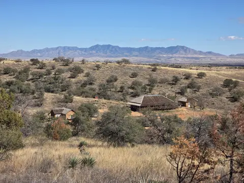 A landscape view of several ranch buildings in a dry, grassy valley with mountains in the background under a blue sky.