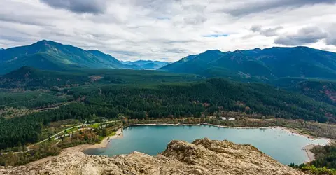 A high-angle view of a lake nestled among forested mountains under a cloudy sky.
