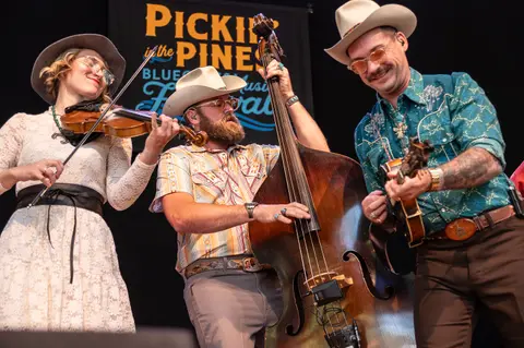 Three musicians perform on stage with string instruments.