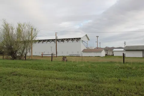 An outdoor view of white buildings and a large open structure under a cloudy sky.