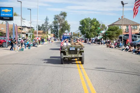 A military jeep drives down a street during a parade with crowds watching on the sides.