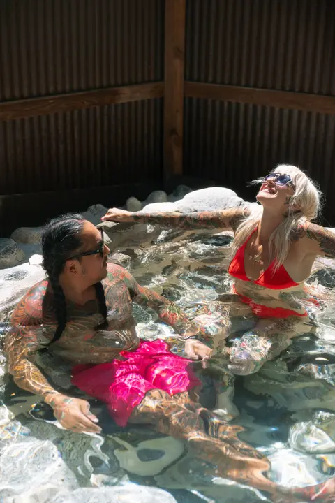 A tattooed man and woman soak together in a hot spring pool.