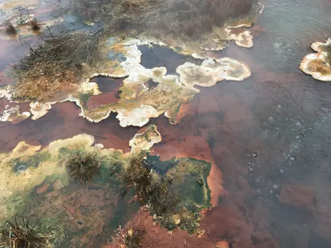 A geothermal feature with colorful mineral deposits and bubbling water.