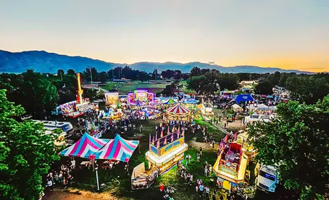An aerial view of a crowded outdoor fair at dusk with rides and tents.