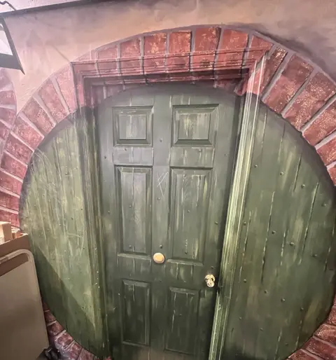 A round green door is set inside a brick archway.
