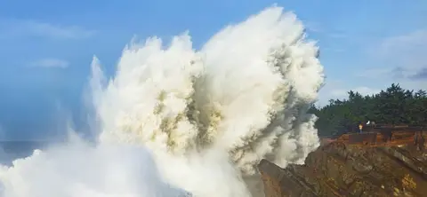 A large wave crashing against rocky cliffs.