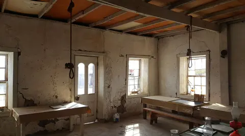 The interior of a rustic historic building with weathered plaster walls, wooden beams, and tables.