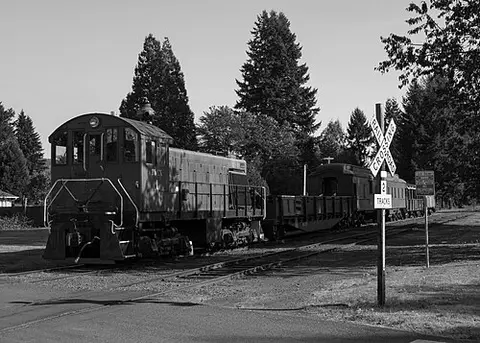 A black and white photo of a train and a railroad crossing sign.
