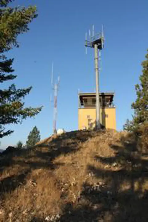 A fire lookout tower stands on a hill with communications towers.