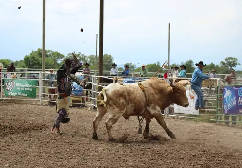 A cowboy is thrown upside down off a bull in an arena.