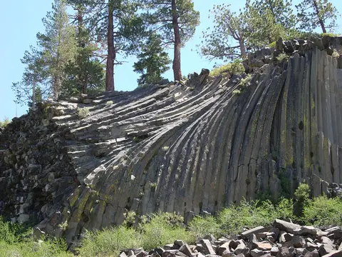 A rock formation featuring vertical basalt columns beneath pine trees.