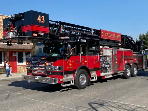 A red and black fire ladder truck parked on an asphalt surface.