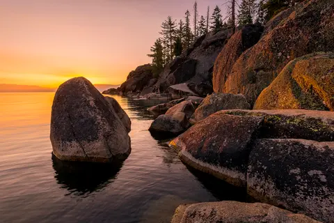 A scenic view of a rocky shoreline and calm water during sunrise.