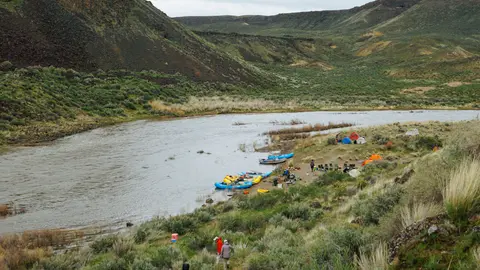 A river flows through a valley with hills and a campsite along the shore.