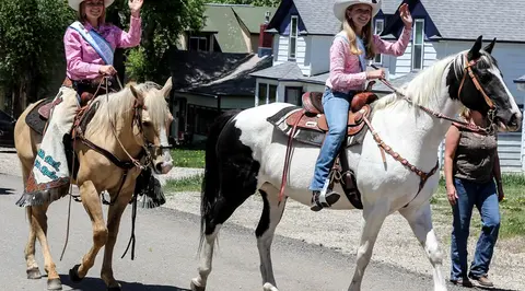 Two young women ride horses down a street.