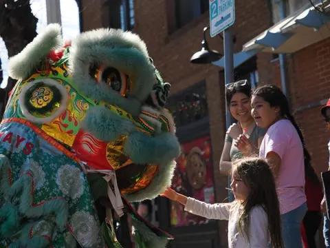 A child reaches out to touch a colorful lion dance costume on a street.