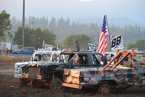 Demolition derby trucks parked in a mud pit with an American flag.