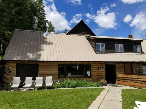 A rustic wooden building with a metal roof stands under a blue sky with white clouds.