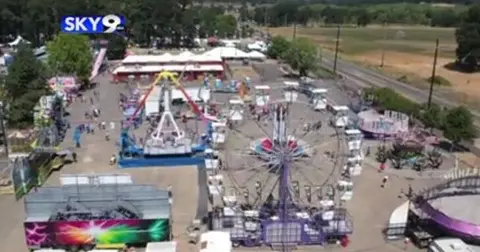 An aerial view shows a carnival with a Ferris wheel and other rides.