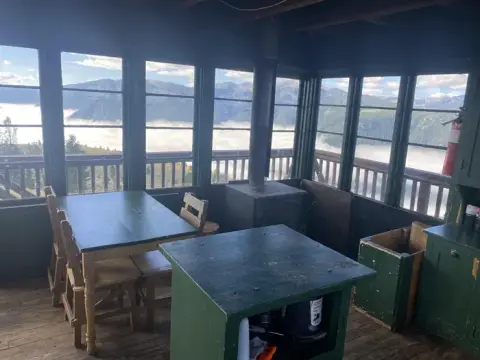 The interior of a lookout cabin with large windows showing a mountain landscape.