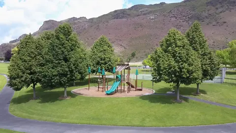 A playground surrounded by lush trees with a mountain in the background.