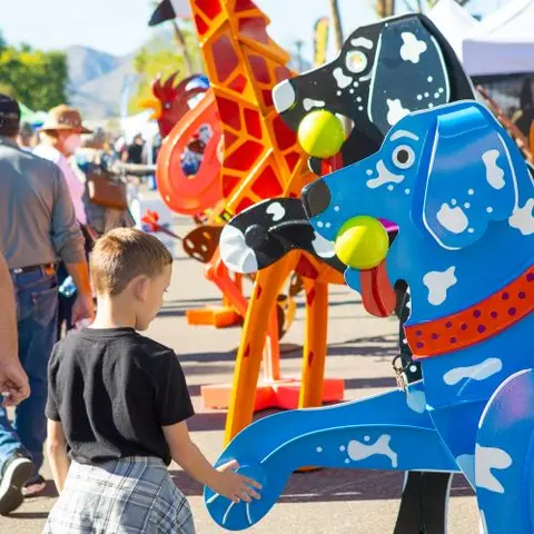 A young boy looks at colorful animal sculptures outdoors.