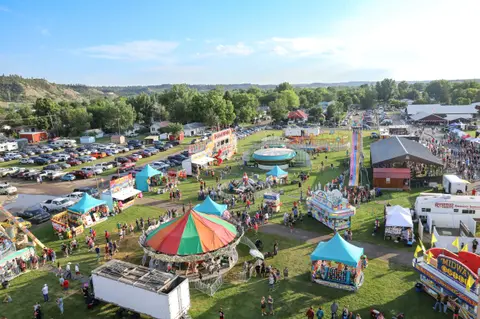 An elevated view of a crowded outdoor fair with rides, booths, and parking.