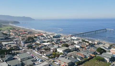 An aerial view of a coastal town next to the ocean with a long pier.