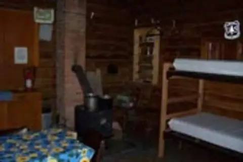 Interior of a rustic cabin with bunk beds and a wood stove.