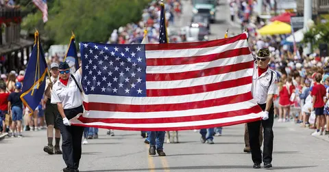 People carry a large American flag down a street during a parade.