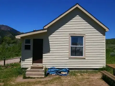 An exterior view of a small light-colored sided building against a clear blue sky.