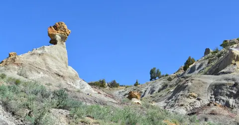 A desert landscape showing unique rock formations and sparse green brush under a blue sky.