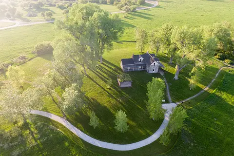 An aerial view of a historic wooden house surrounded by trees and green fields.