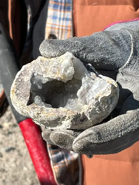 A person wearing gloves holds a hollow geode filled with crystals.