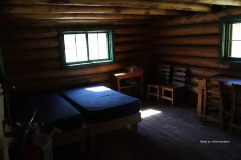 An interior view of a rustic log cabin with beds and wooden furniture.
