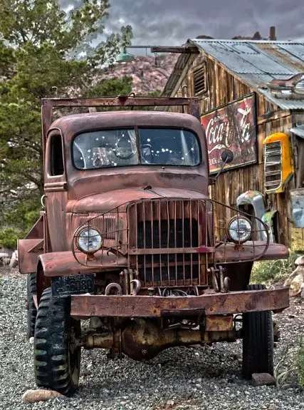 An old rusty truck parked in front of a weathered wooden building.