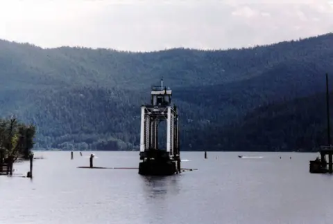 A structure stands in the middle of a lake with forested mountains in the background.