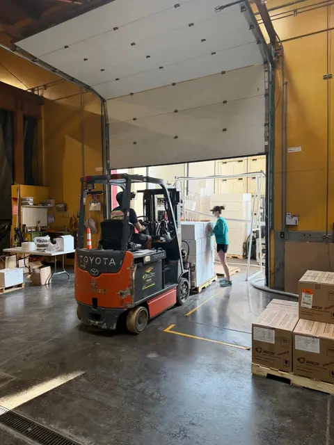 A forklift operates inside a warehouse near an open loading door.